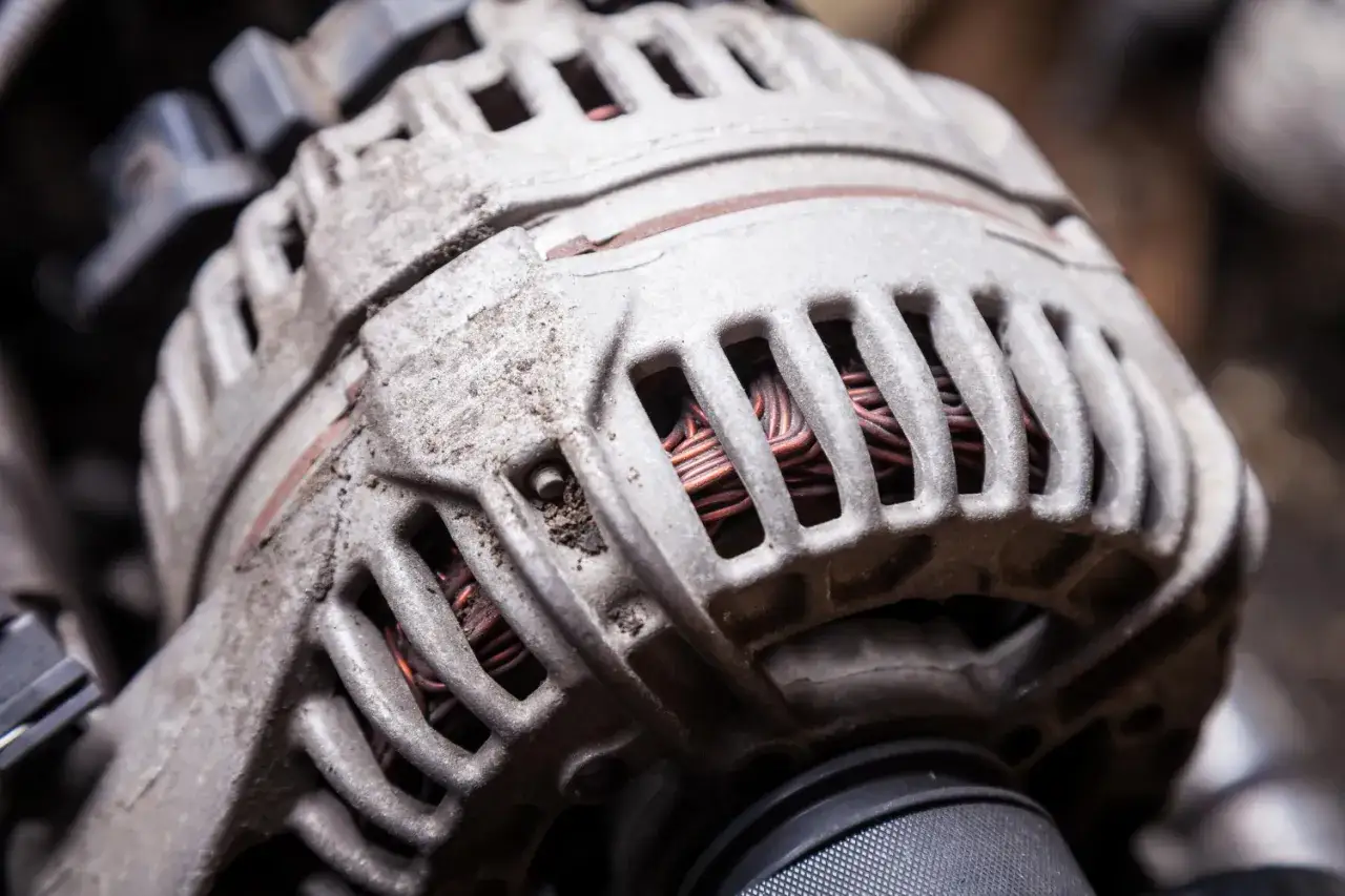 Zbliżenie na zużyty alternator samochodowy z widocznymi miedzianymi uzwojeniami.