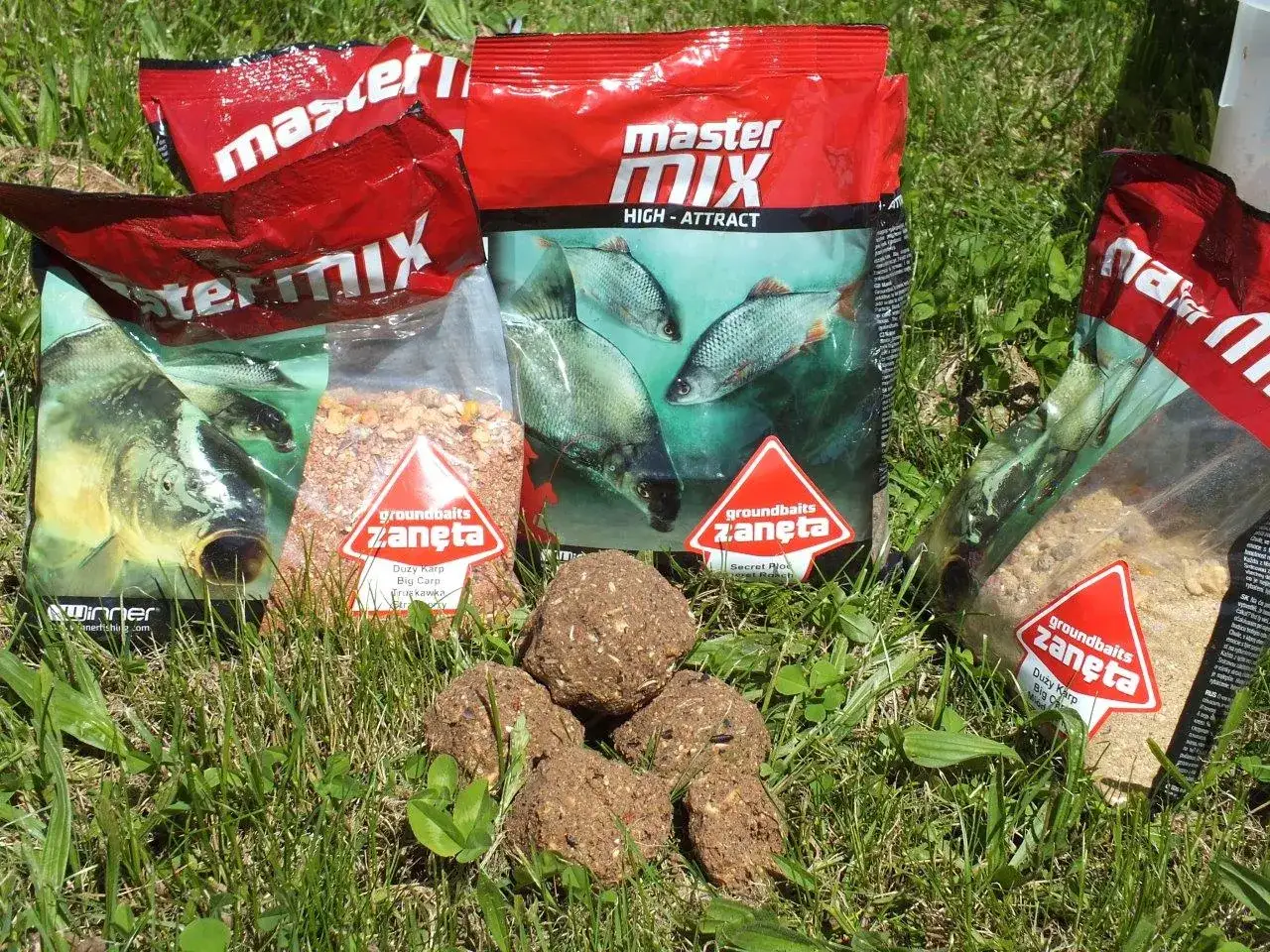 Kilka opakowań zanęta wędkarska 10kg i kulki proteinowe na trawie.