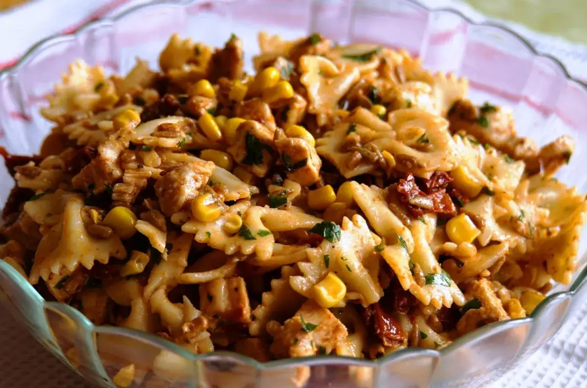 Pyszna sałatka z kurczakiem i makaronem farfalle, kukurydzą i suszonymi pomidorami, posypana natką pietruszki.