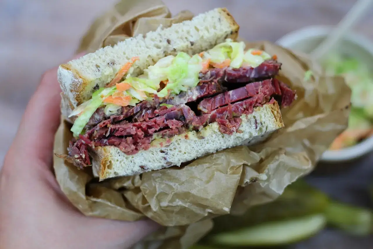 Pyszna kanapka z pastrami, z chrupiącą surówką i musztardą, zawinięta w papier.