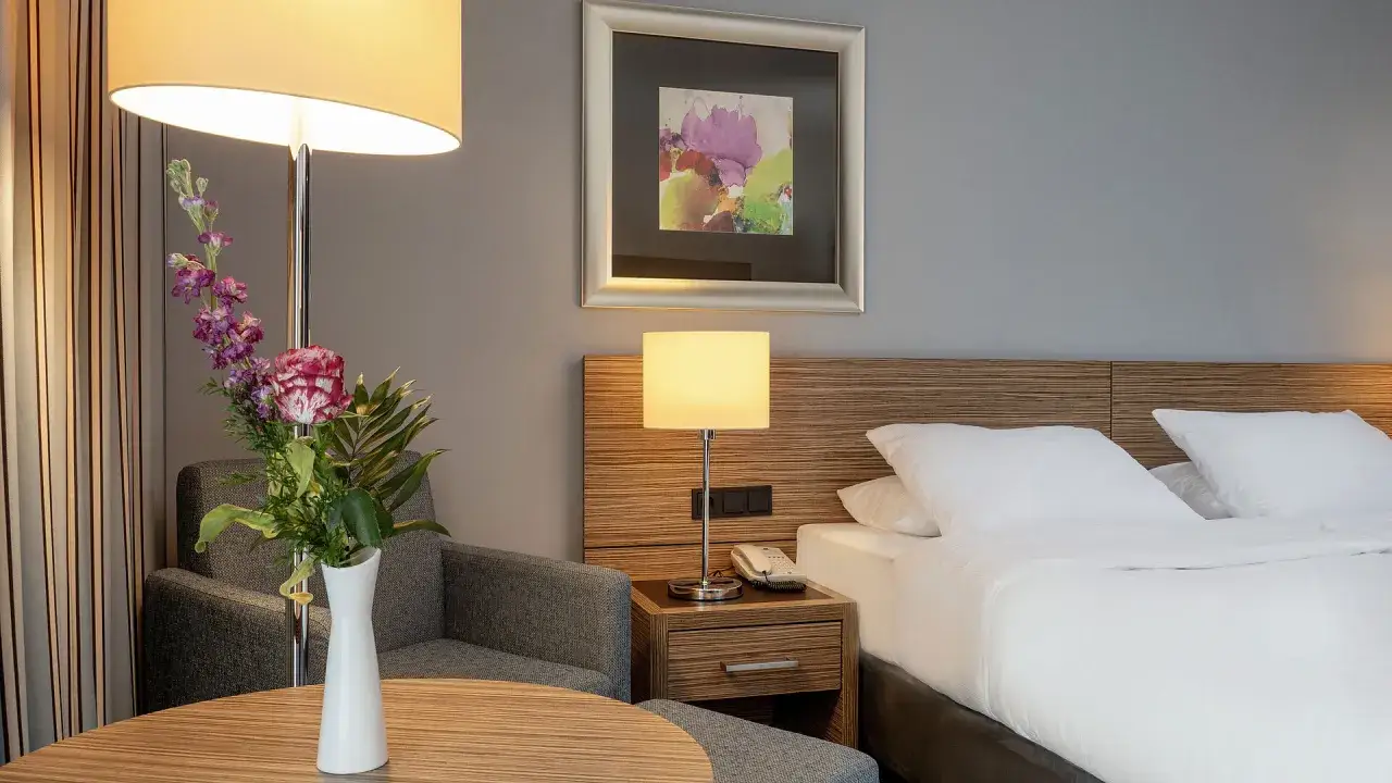 Ein Hotelzimmer mit Bett, Nachttischlampe, Sessel und Blumenstrauß.