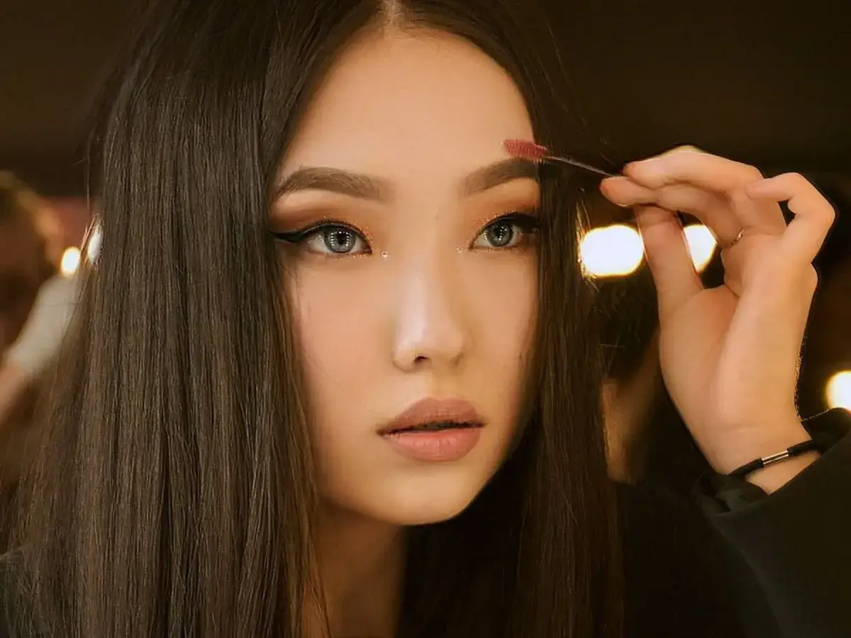 Kobieta z ciemnymi włosami i makijażem oczu delikatnie poprawia brwi szczoteczką. Może to być część procesu, jak rozjaśnić brwi po hennie.