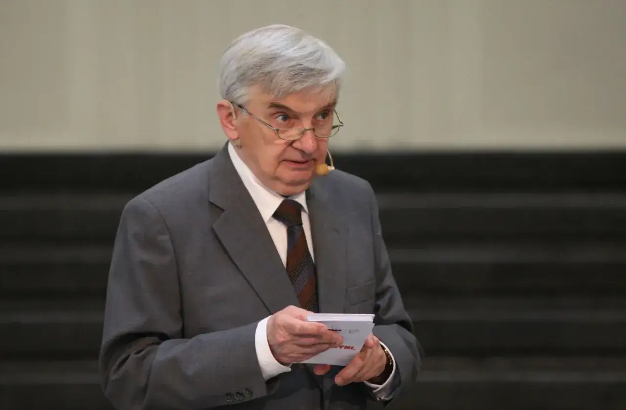 Starszy mężczyzna w garniturze, który prowadzi jeden z dziesięciu, trzyma kartkę.