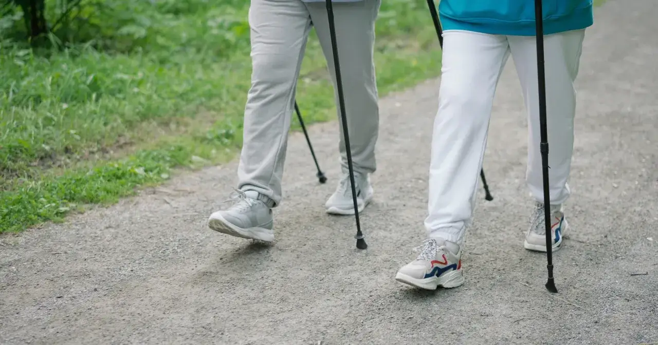 Dwie osoby idące z kijkami po leśnej ścieżce. Pokazują, jak chodzić z kijkami, czerpiąc radość z aktywności na świeżym powietrzu.
