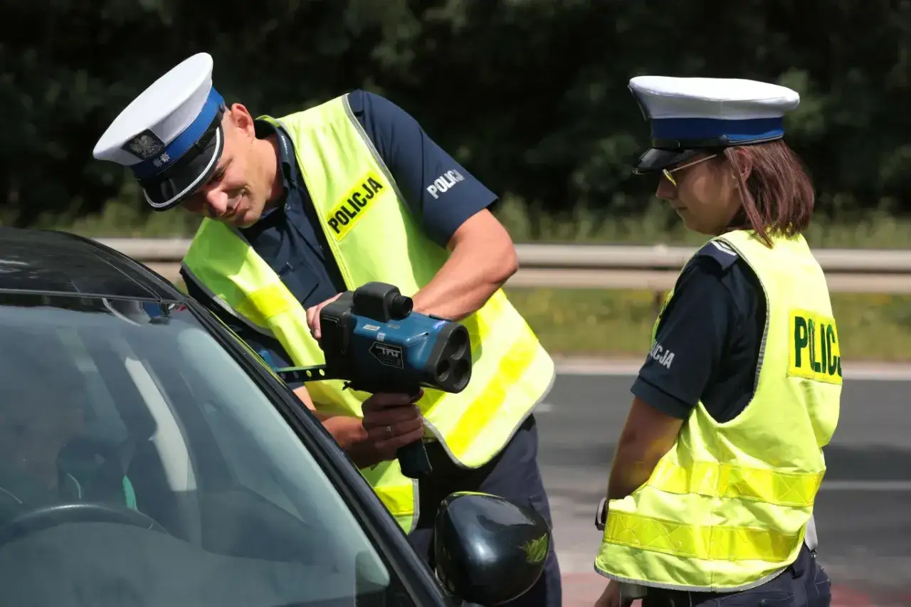 Policjanci w kamizelkach odblaskowych mierzą prędkość samochodu radarem.