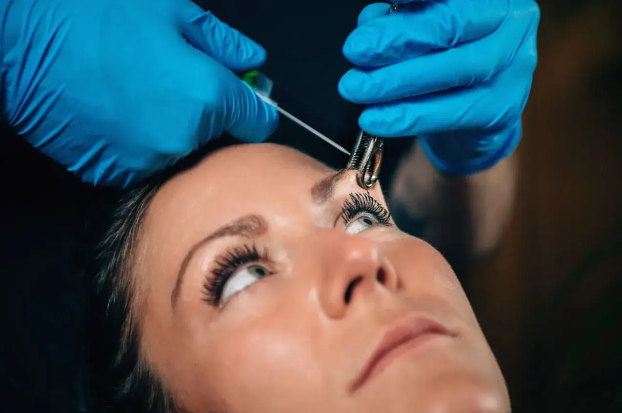 Osoba w niebieskich rękawiczkach wykonuje kolczyk w brwi.