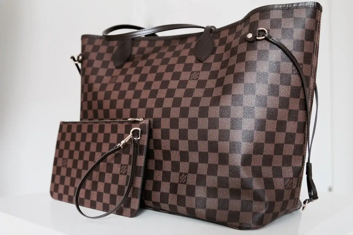 Duża torebka Louis Vuitton w kratkę, obok mniejsza kosmetyczka. Klasyczny wzór Damier Ebene.