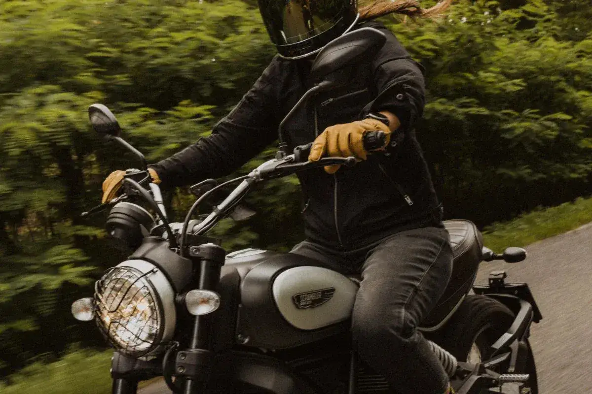 Motocyklista w kasku i rękawiczkach jedzie motocyklem. W tle zielony las. To świetny moment, by nauczyć się, jak zmieniać biegi w motorze.