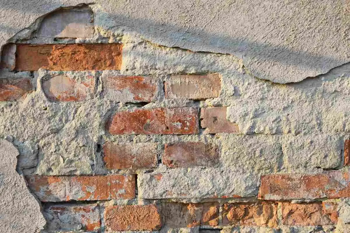 Fragment starego muru z cegły z odpadającym tynkiem.