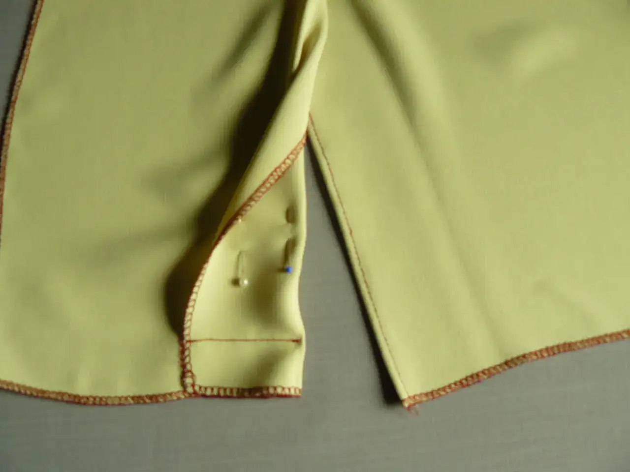 Szczegółowy widok na żółtą sukienkę, pokazujący, jak zrobić rozporek. Widoczne szpilki i czerwone obszycie.