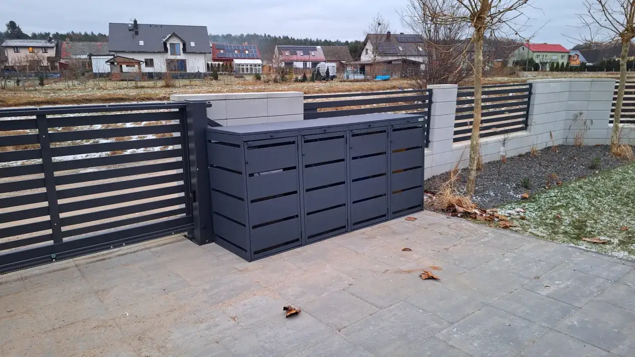 Nowoczesne, ciemnoszare miejsce na kosze na śmieci w ogrodzeniu, z widokiem na domy i zimowy krajobraz.
