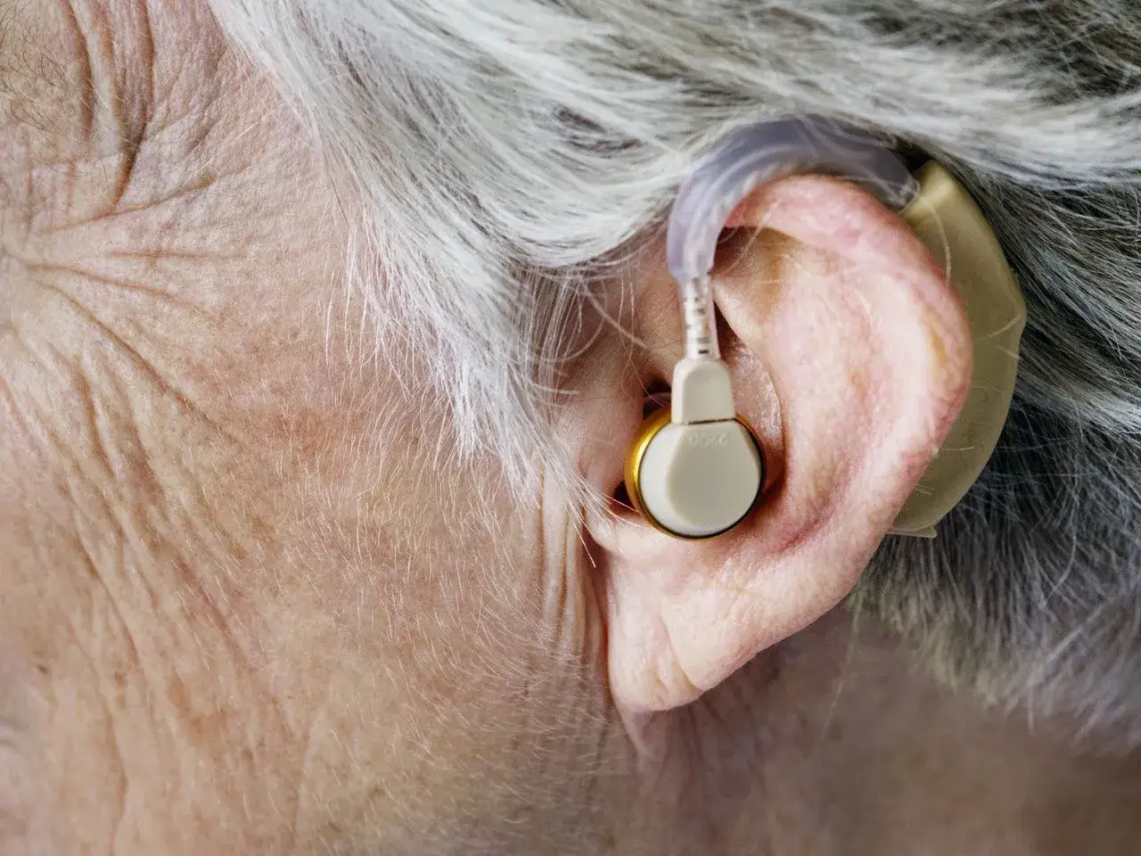 Ucho starszej osoby z aparatem słuchowym. Zastanawiasz się, ile kosztuje dobry aparat słuchowy?