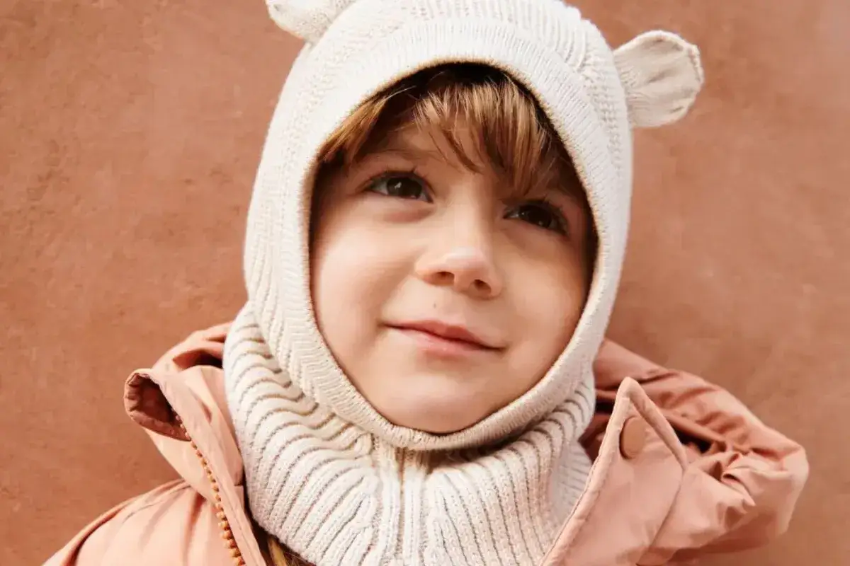 Uśmiechnięte dziecko w beżowej czapce z uszkami i różowej kurtce.