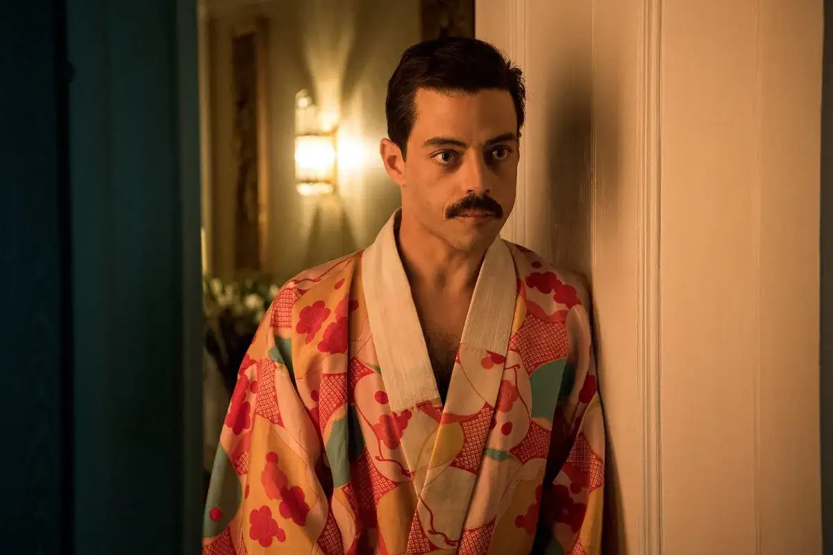 Freddie Mercury w barwnym szlafroku, jakby zrodzony z **bohemian rhapsody**, opiera się o drzwi.