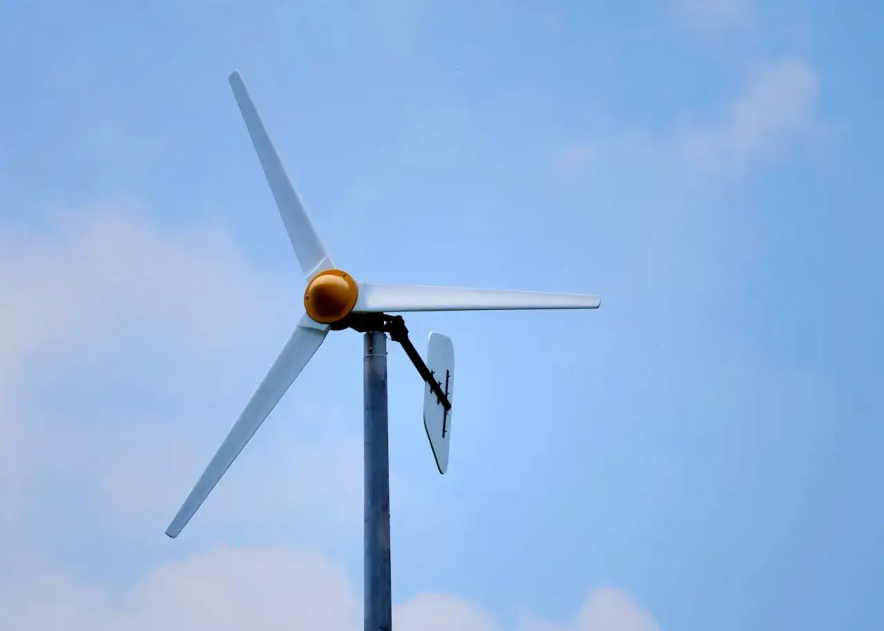 Biała elektrownia wiatrowa z żółtym elementem na środku, na tle błękitnego nieba z chmurami.