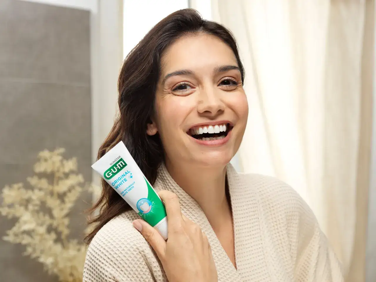 Uśmiechnięta kobieta trzymająca pastę GUM Original White. Dbanie o dziąsła (gum care) to klucz do pięknego uśmiechu.