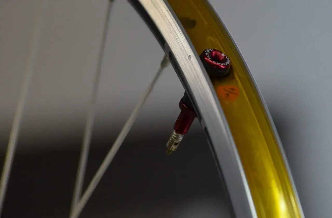 Koło rowerowe z wentylem do opon bezdętkowych. Czerwona nakrętka wentyla i złota obręcz.