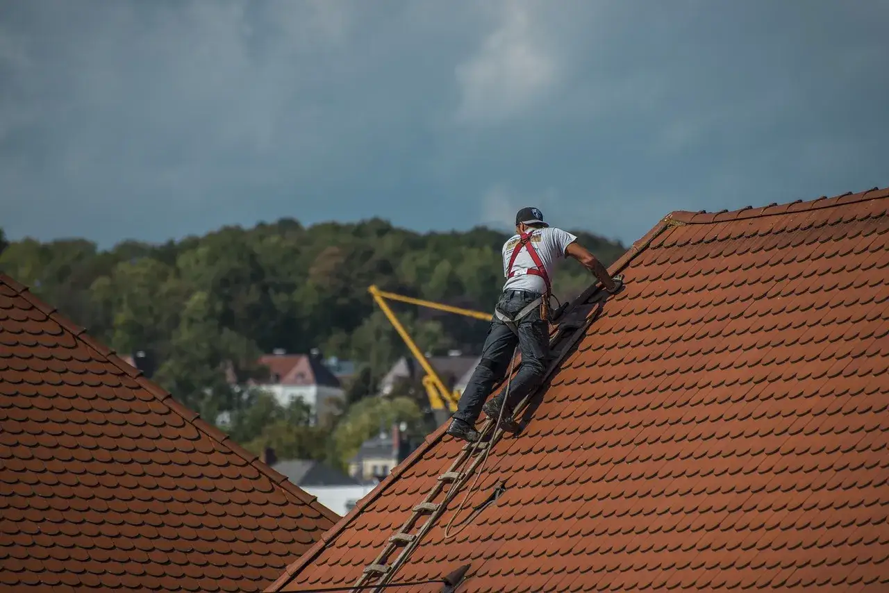 Dekarz w szelkach asekuracyjnych pracuje na czerwonym dachu.