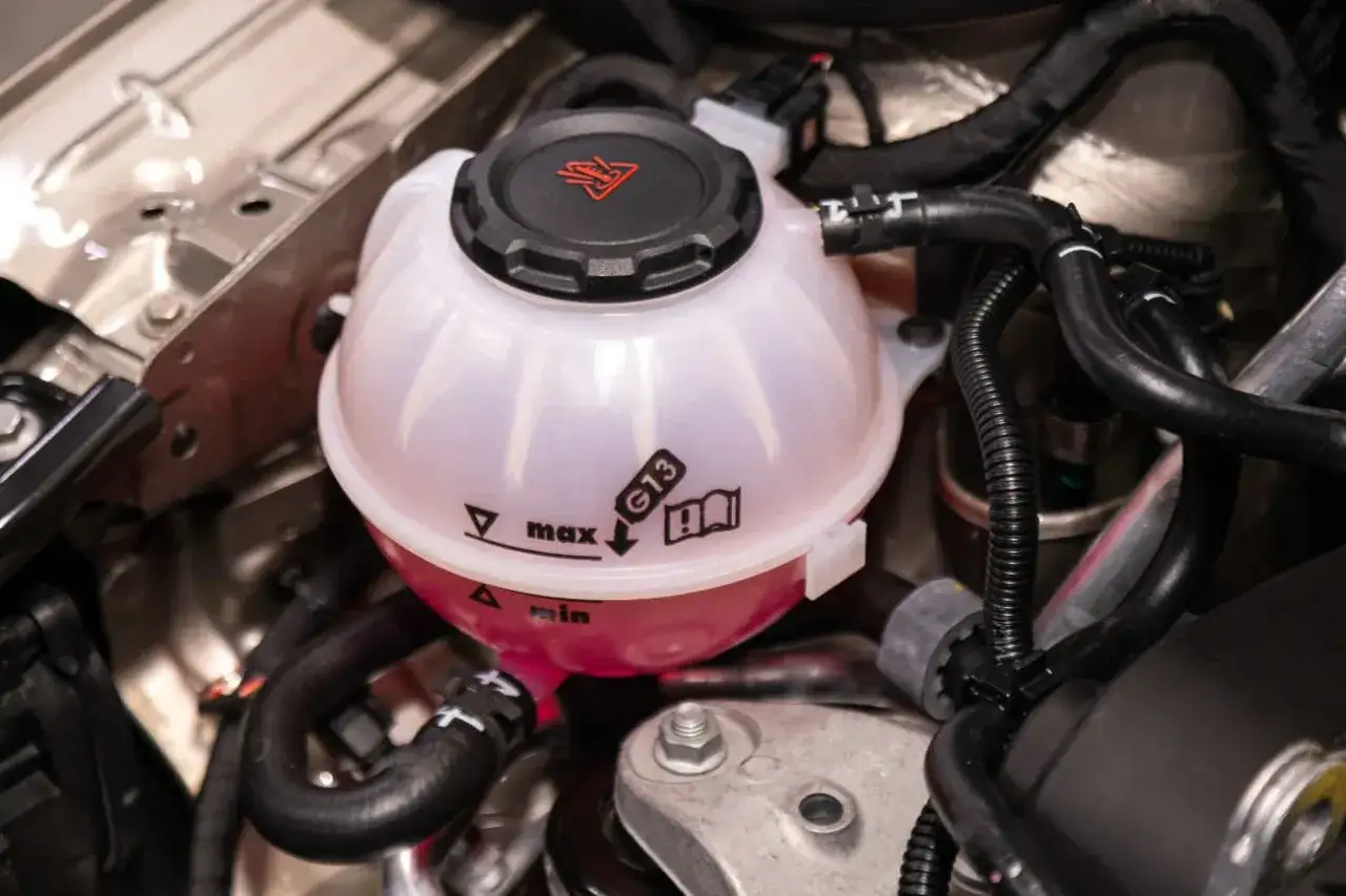 Zbiorniczek płynu chłodniczego z widocznym niskim poziomem płynu poniżej oznaczenia "min". Wskazuje to na ubytek płynu chłodniczego.