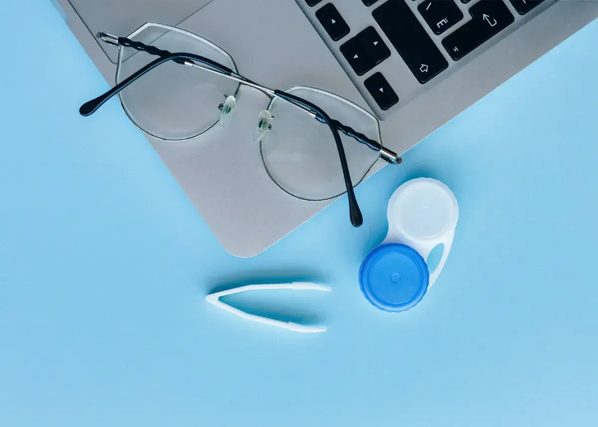 Okulary, pojemnik na soczewki i pęseta leżą obok laptopa. Czy można nosić soczewki i okulary jednocześnie?