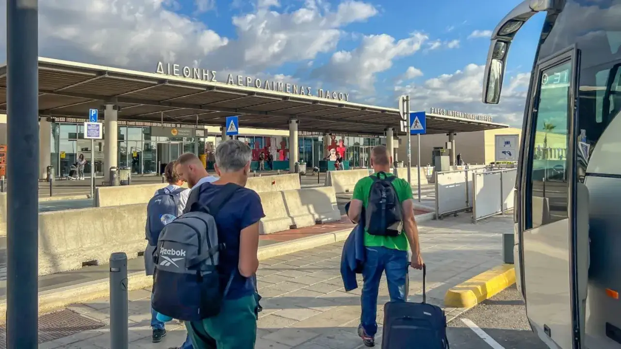 Ludzie z bagażami wychodzą z autobusu na lotnisku w Pafos. Czy na Cyprze jest bezpiecznie? Tak, podróżni bezpiecznie docierają do celu.