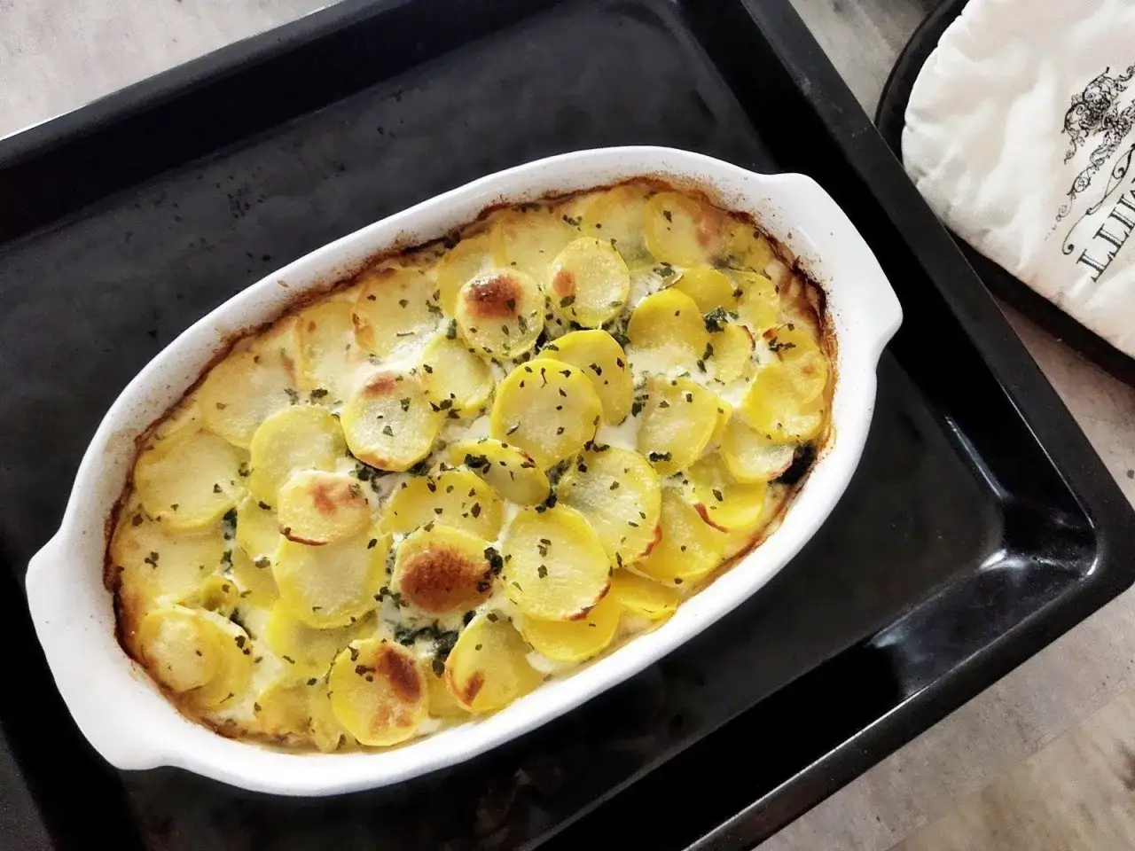 Zapiekanka ziemniaczana w kremowym sosie, posypana ziołami. Idealne danie, gdy zastanawiasz się, co na obiad tanio i smacznie.