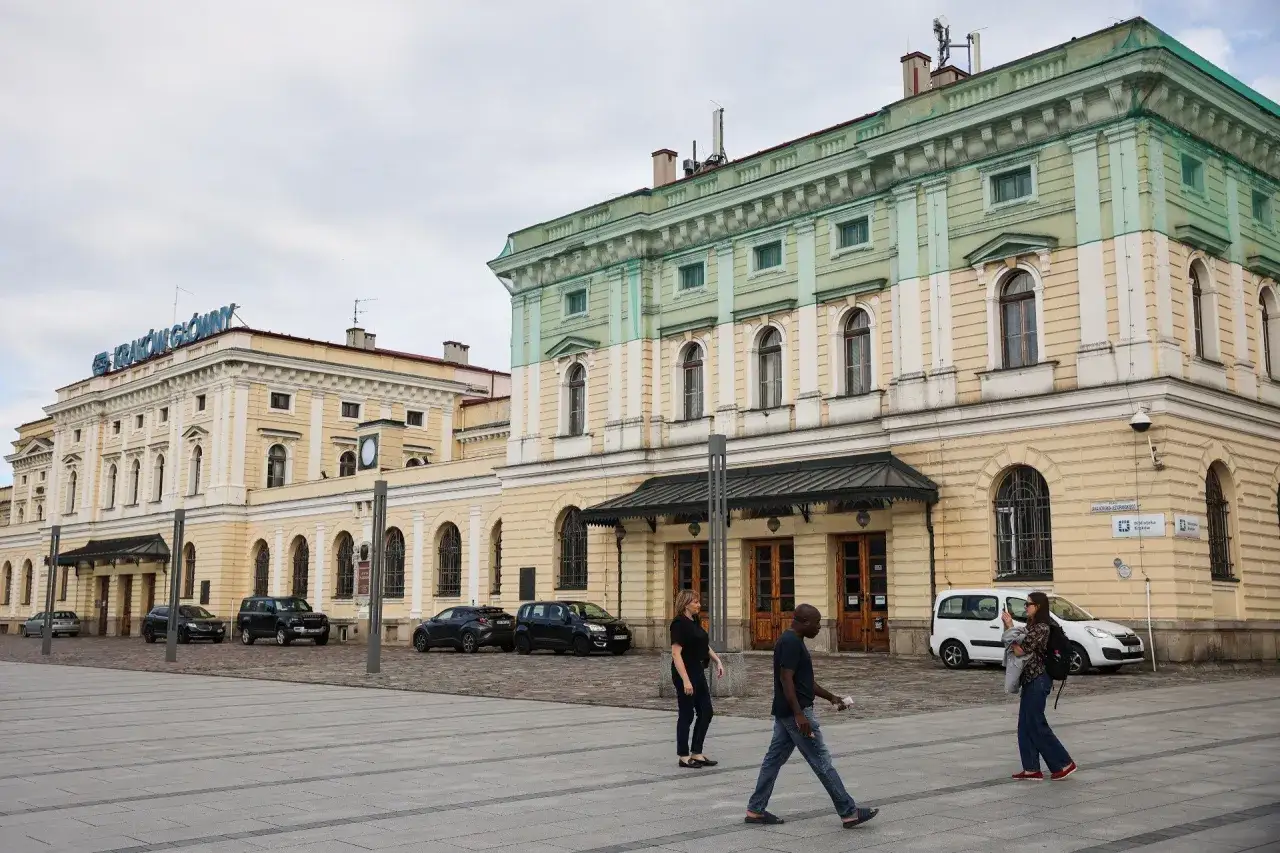 Kraków Główny. Krótki spacer z dworca na rynek, przez plac przed zabytkowym budynkiem, gdzie przechodzą ludzie.