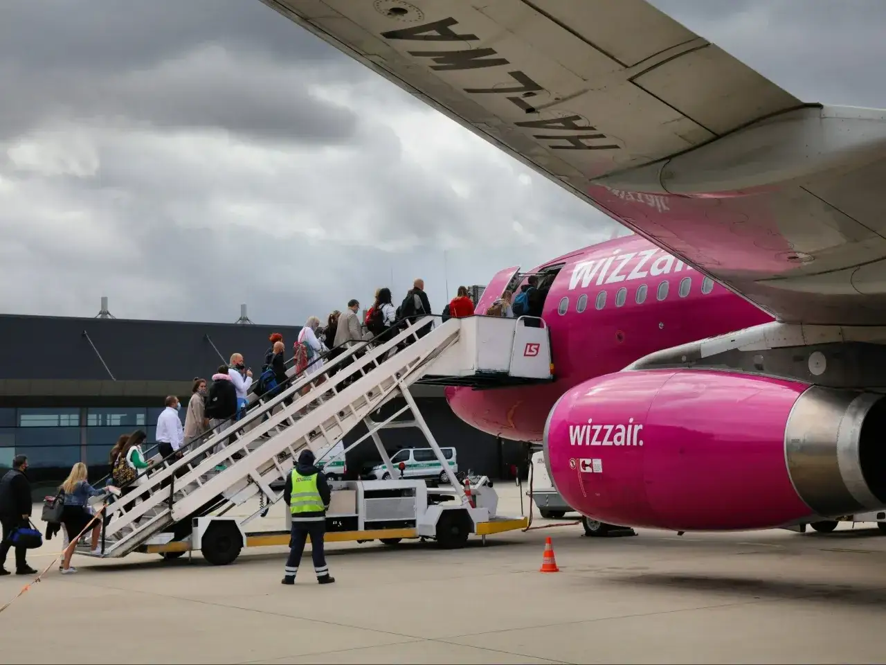 Pasażerowie wsiadają po schodkach do różowego samolotu Wizz Air.