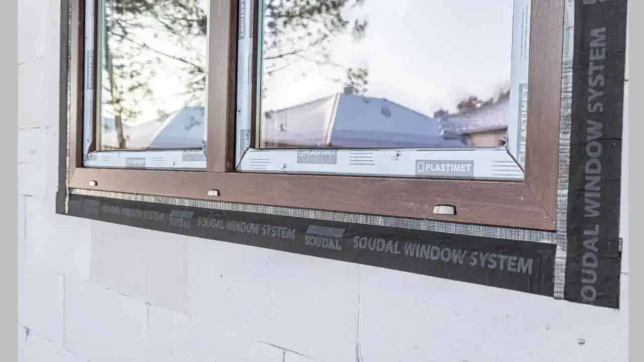 Ciepły montaż po zamontowaniu okien. Widoczna taśma Soudal Window System wokół drewnianej ramy okiennej w białej ścianie z bloczków.