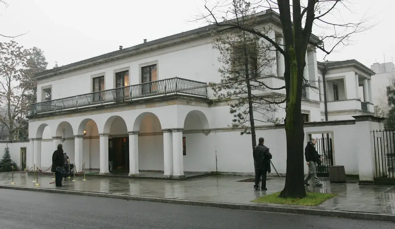 Biała willa z arkadami, gdzie mieszka Donald Tusk. Na zewnątrz widać kilka osób i drzewa.