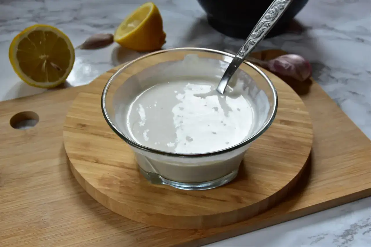 Kremowy sos aioli w szklanej miseczce, obok cytryny i czosnku. Idealny dodatek do dań.
