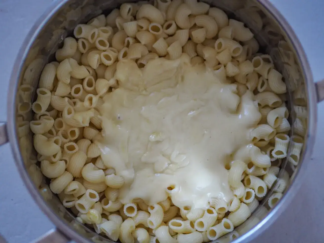 Gęsty, kremowy sos serowy otula makaron w garnku, tworząc pyszny makaron mac and cheese.
