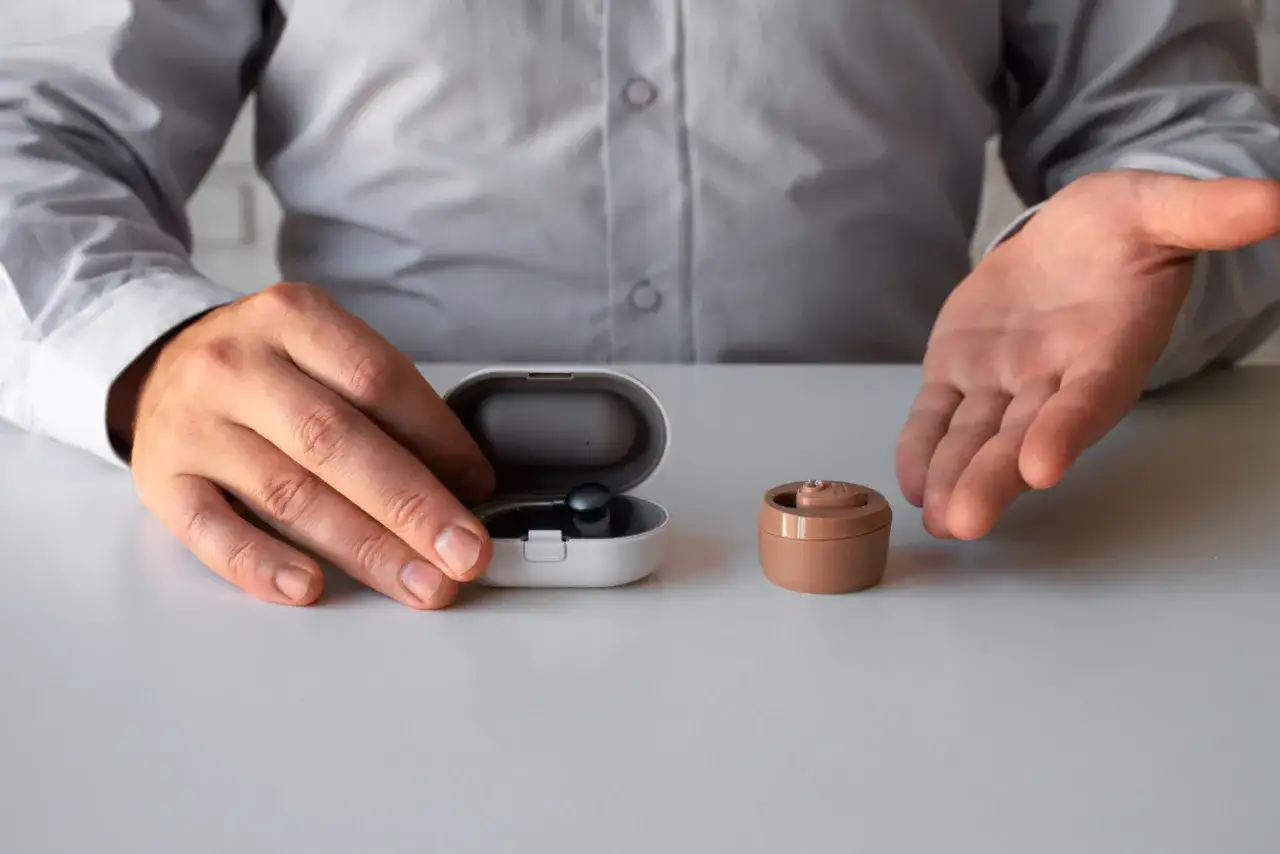 Dłonie mężczyzny prezentują aparaty słuchowe i etui. Zastanawiasz się, dlaczego aparat słuchowy szumi?