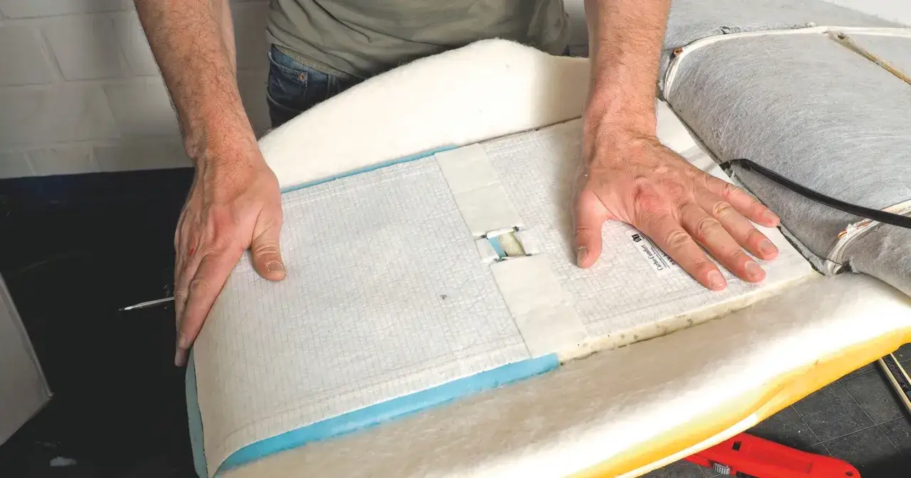 Naprawa podgrzewania foteli: montaż maty grzewczej pod tapicerką. Dłonie układają element grzewczy na piance fotela.