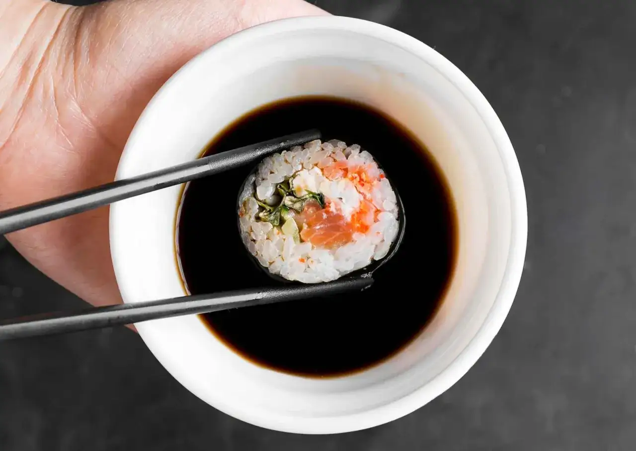 Pałeczki trzymają sushi z łososiem, zanurzając je w miseczce z gęstym słodkim sosem do sushi.