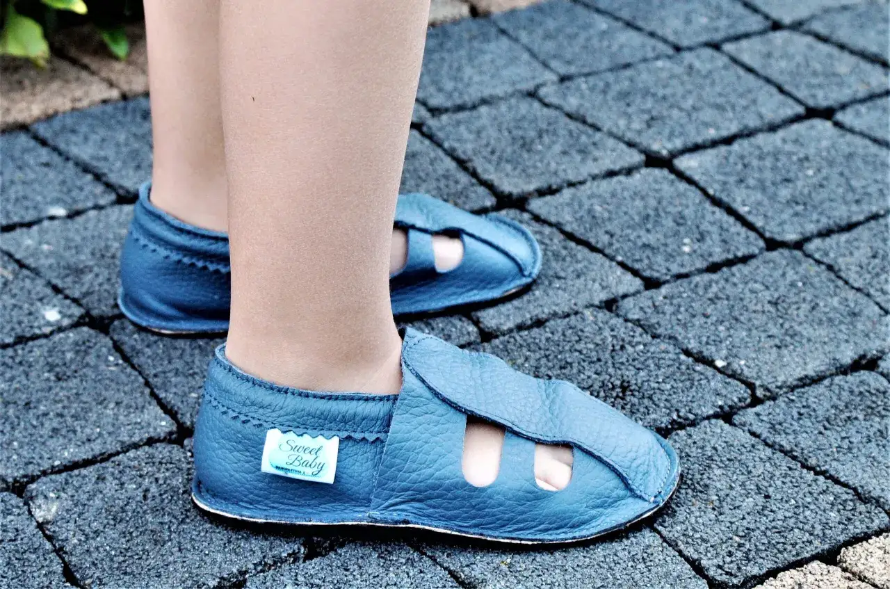 Niebieskie skórzane kapcie dziecięce z otworami na palce na tle kostki brukowej.