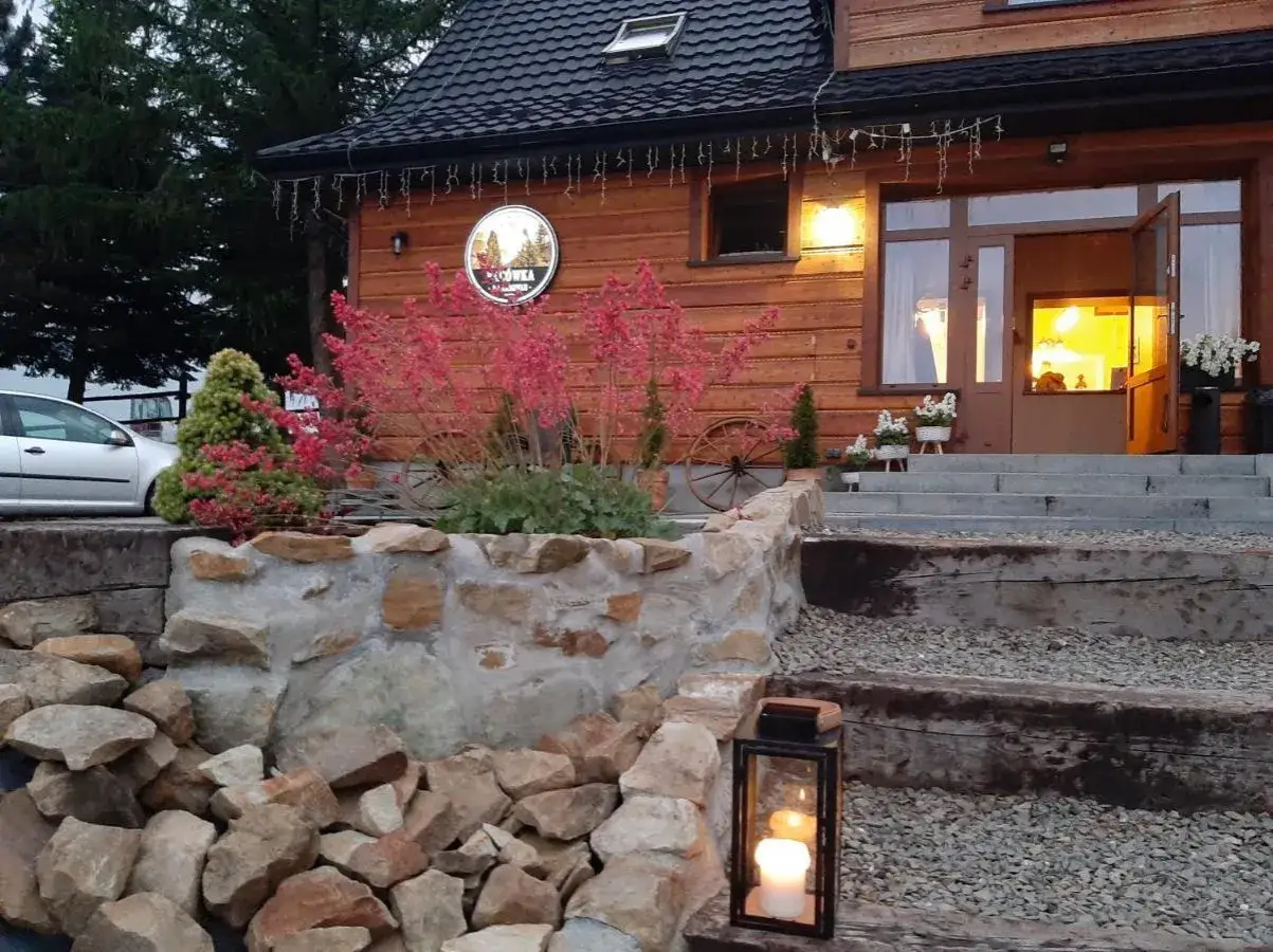 Przytulna bacówka na zadzielu wita gości. Drewniany dom, kamienny murek i kwitnące kwiaty tworzą sielski klimat.