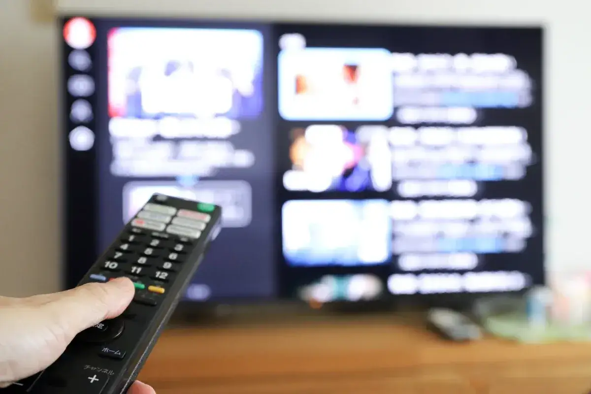 Dłoń z pilotem przed ekranem telewizora, na którym widać menu aplikacji. Dowiedz się, jak ściągnąć aplikację na telewizor.