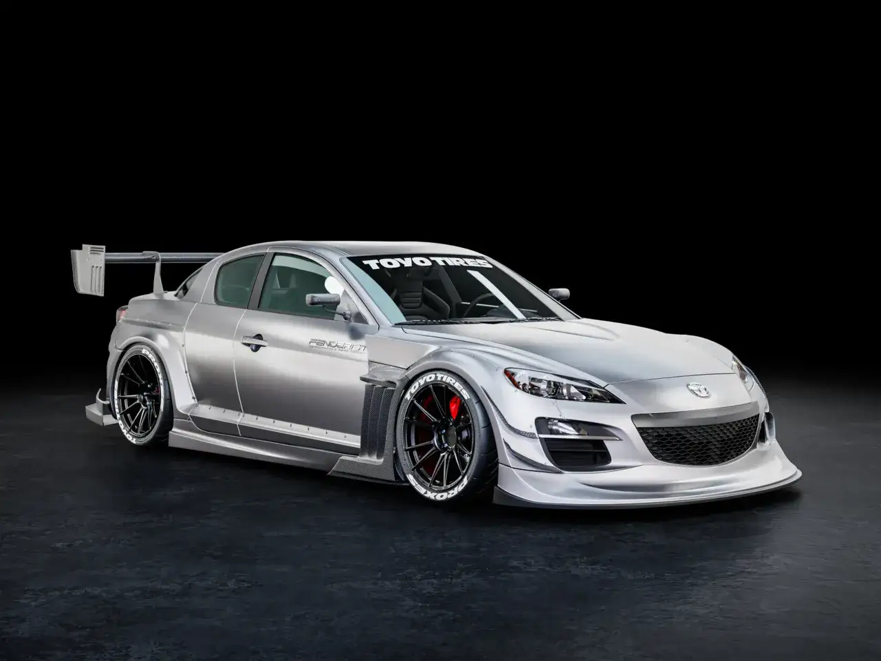 Srebrna Mazda RX8 z agresywnym body kitem, szerokimi błotnikami, spojlerem i felgami Toyo Tires.