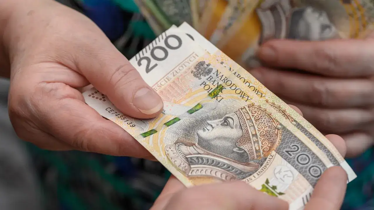 Dwie dłonie przekazują sobie banknot 200 zł. Czy opieka nad dzieckiem niepełnosprawnym wlicza się do emerytury?