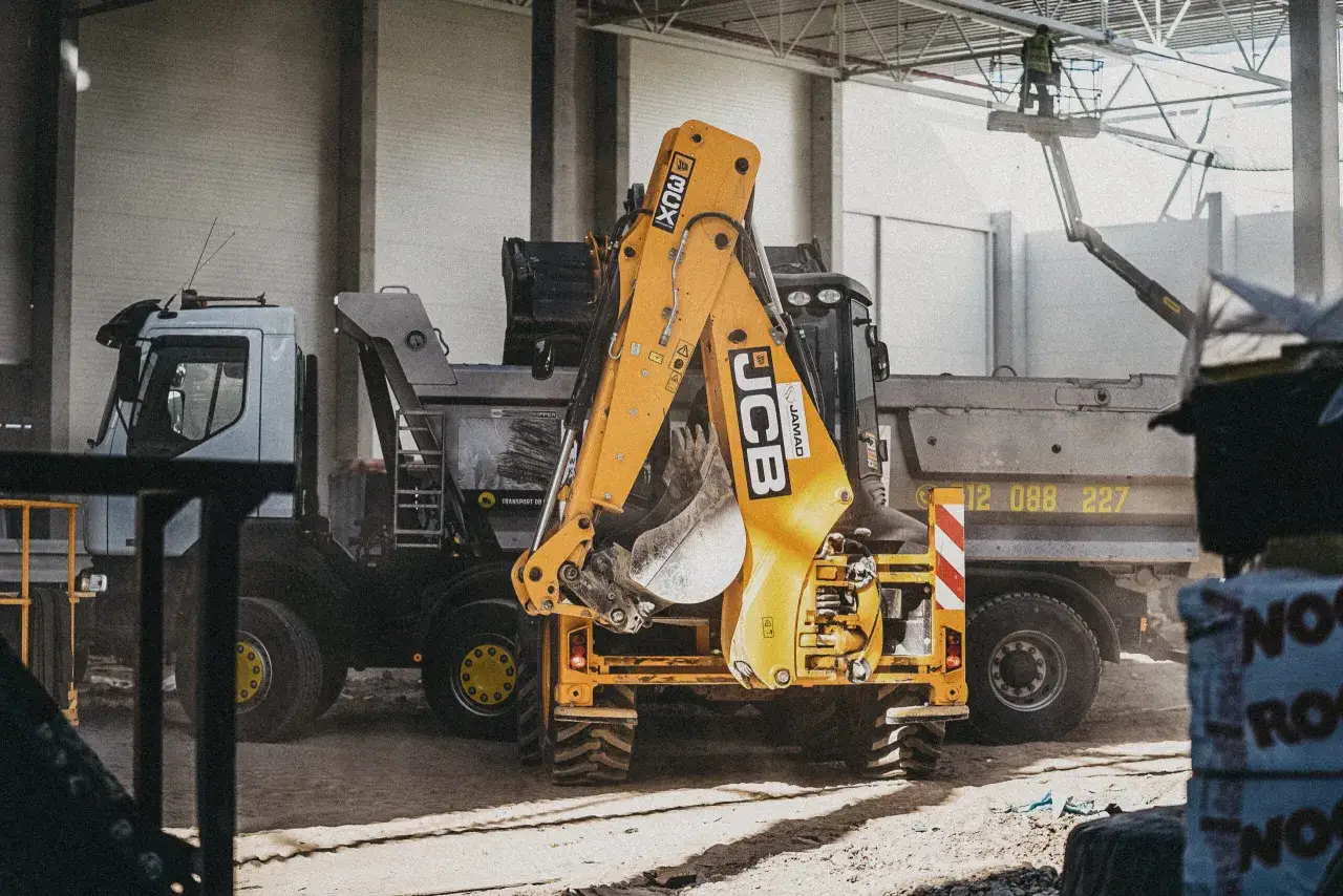 Żółty koparko-ładowarka JCB i ciężarówka na placu budowy.