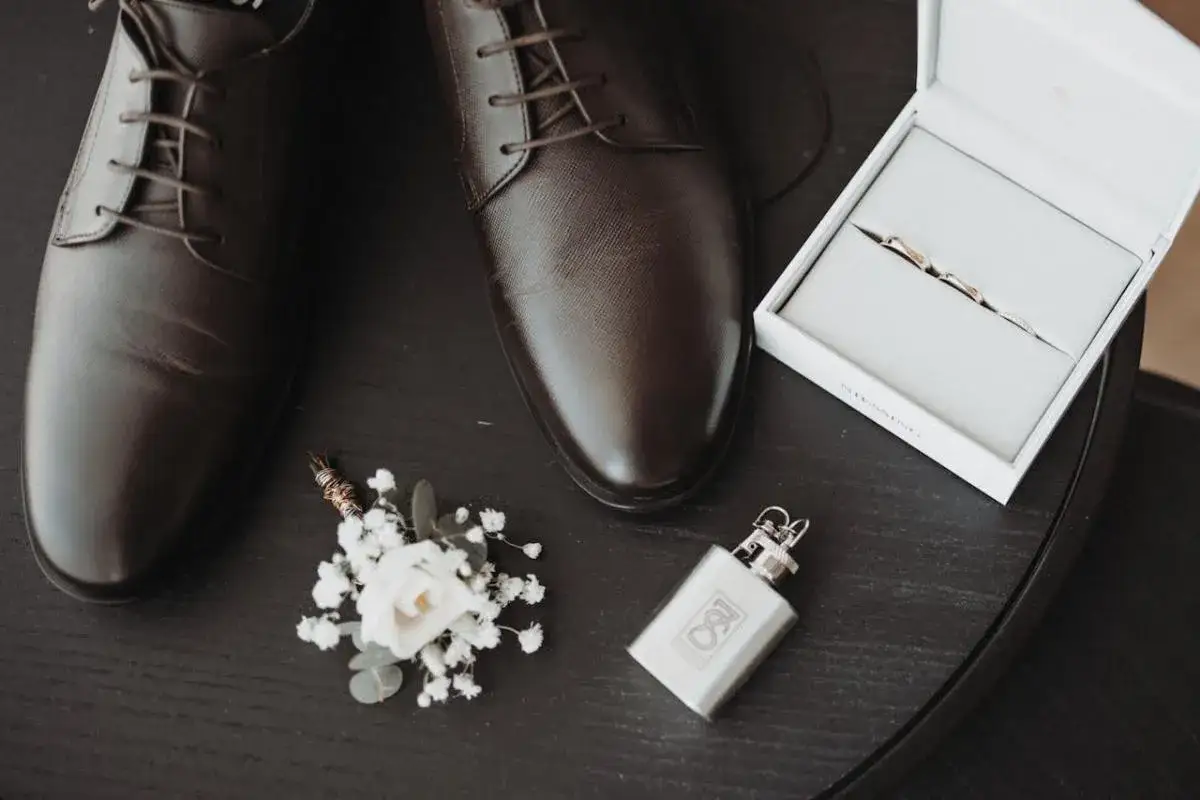 Eleganckie brązowe buty męskie, butonierka, pierścionki w pudełku i piersiówka.