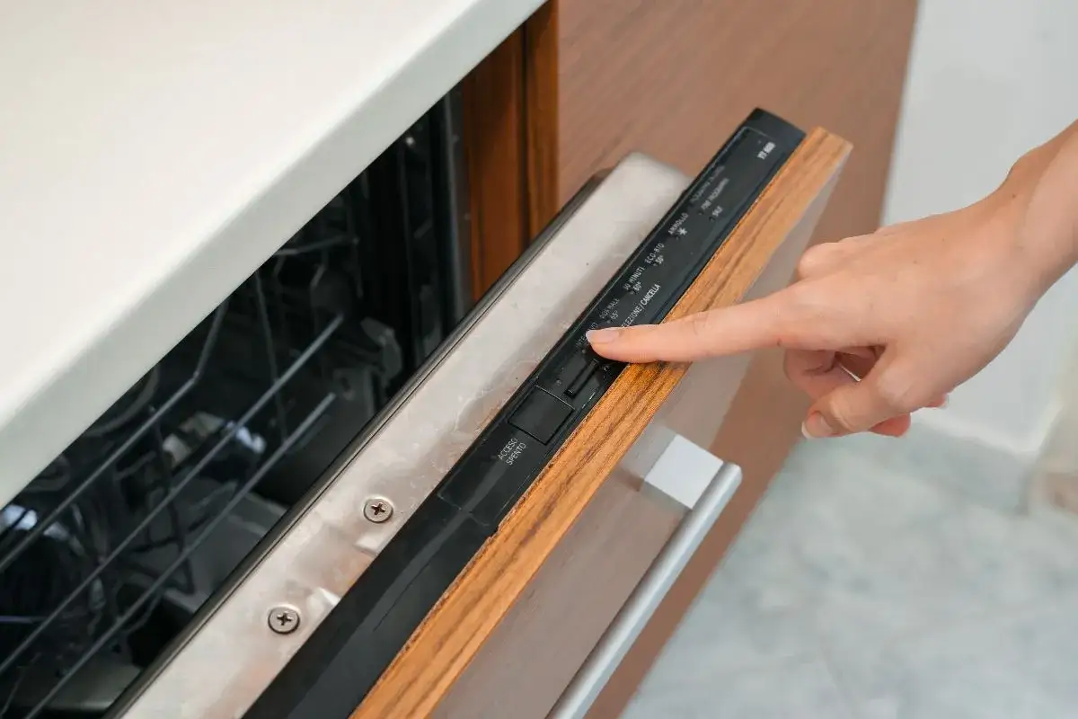 Dłoń naciska przycisk na panelu zmywarki, pokazując, co oznaczają symbole na zmywarce.