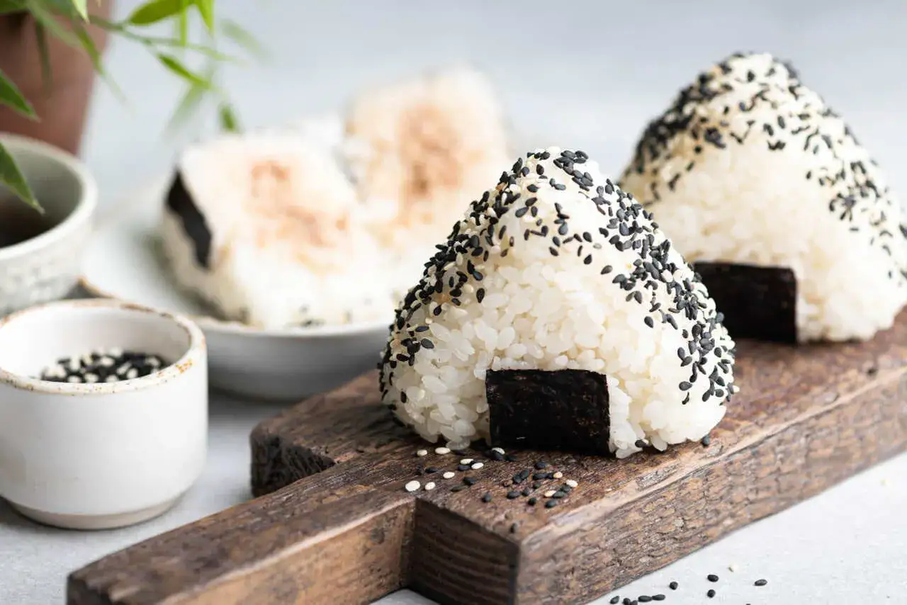Trójkątne onigiri sushi z czarnym sezamem i kawałkiem nori na drewnianej desce.