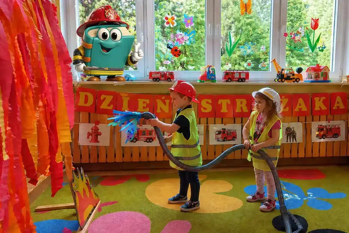 Dzieci gaszą pożar, świetne pomysły na dni otwarte w przedszkolu! Maskotka-książka w stroju strażaka zachęca do zabawy.