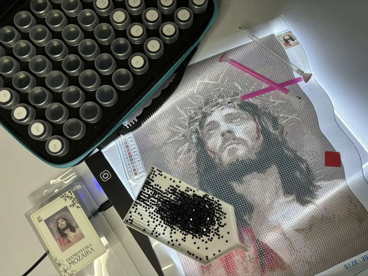 Zestaw do haftu diamentowego: płótno z wizerunkiem Jezusa, pojemniczki z diamencikami, tacka i pisaki. Jak zrobić haft diamentowy?