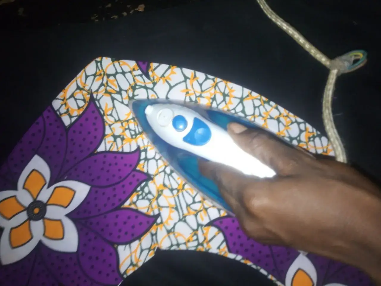 Dłoń prasuje żabot z kolorowym wzorem kwiatowym.