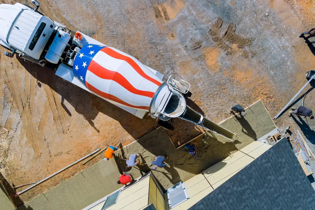Betonowanie fundamentów pod dom. Ekipa budowlana pracuje przy wylewaniu betonu z betoniarki.