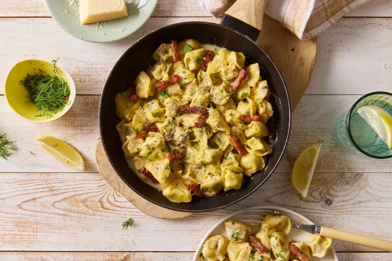 Tortellini z mięsem w kremowym sosie z boczkiem, posypane natką pietruszki i parmezanem, podane z cytryną.