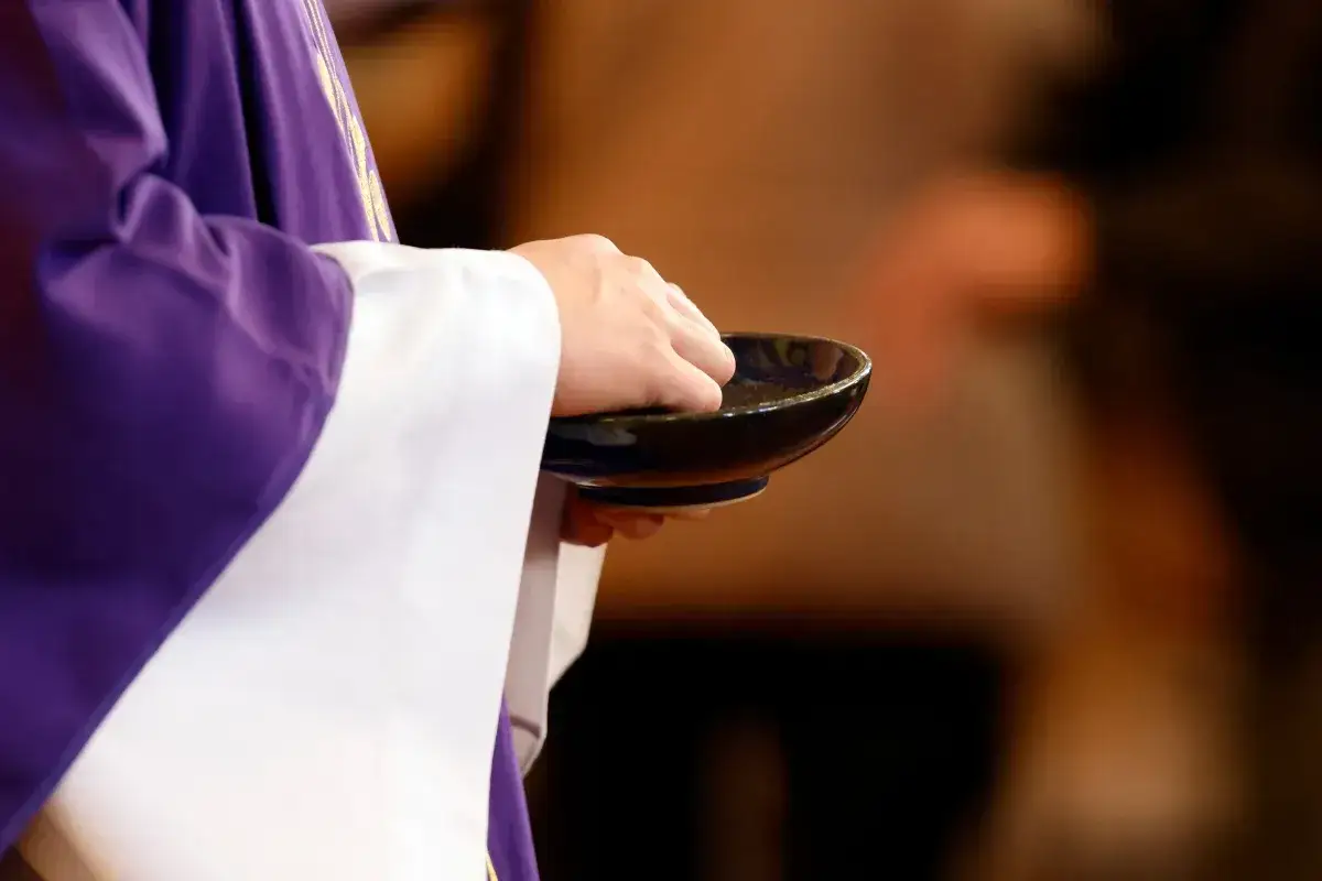 Kapłan w fioletowej dalmatyce podczas mszy świętej w środę popielcową zanurza palce w miseczce z popiołem.